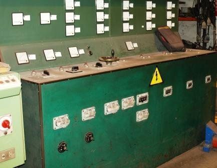 Panel de control eléctrico industrial con varios indicadores, interruptores y una señal de advertencia amarilla en una consola metálica verde.