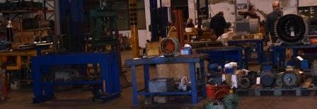 El interior de un taller con bancos de trabajo azules, equipos industriales y personas trabajando con maquinaria.