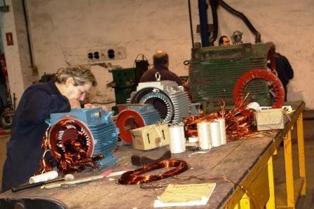 En un taller, una persona trabaja en la reparación de un motor eléctrico industrial con bobinas de alambre de cobre sobre un banco de trabajo.