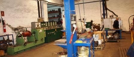 Un taller con una máquina industrial verde, un soporte azul y una persona caminando al fondo.