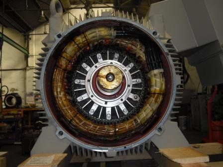 Vista interior de un motor eléctrico industrial con bobinados de cobre visibles y conjunto de rotor central en un taller.