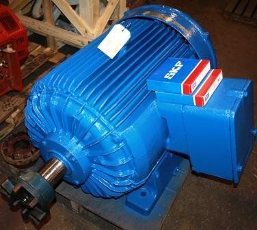 Un gran motor eléctrico azul descansa sobre un palé de madera, con cajas de la marca SKF apoyadas sobre su caja de terminales.