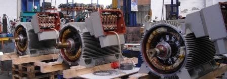 En un taller, tres grandes motores eléctricos industriales se encuentran uno al lado del otro sobre paletas de madera.