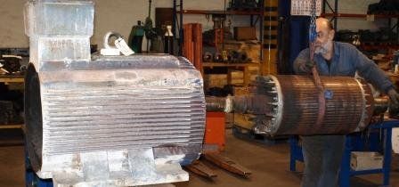 En un taller mecánico, un operario utiliza un polipasto para alinear el rotor de un motor de gran tamaño con su carcasa.