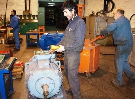Tres trabajadores de un taller realizan tareas de mantenimiento en un gran motor eléctrico industrial.