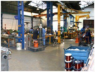 En el interior de un taller industrial, los empleados trabajan en puestos situados cerca de columnas de soporte azules y bobinas de alambre de cobre.