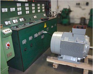 Un gran motor eléctrico gris conectado a una consola de control industrial verde con numerosos diales e indicadores en un taller.