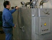 Una persona con una chaqueta azul manejando una gran máquina industrial de metal gris en un taller.