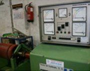 Un panel de control con cuatro indicadores analógicos montado sobre la base de una máquina industrial de color verde, con un extintor de incendios cerca.