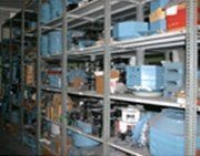 Estanterías metálicas en un almacén repleto de diversos equipos industriales y componentes azules.