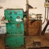 En un taller se encuentra un torno industrial de metalurgia de color verde, con perillas de control en su panel frontal.