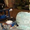 Un motor eléctrico de color claro se alza en primer plano en un taller industrial desordenado.