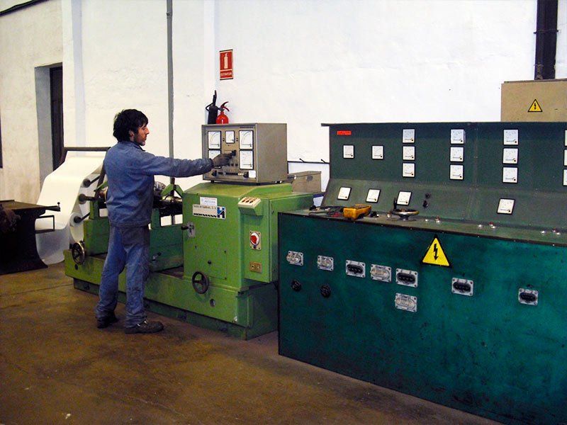 Un trabajador vestido de azul maneja una máquina industrial verde con paneles de control en un taller de fábrica.