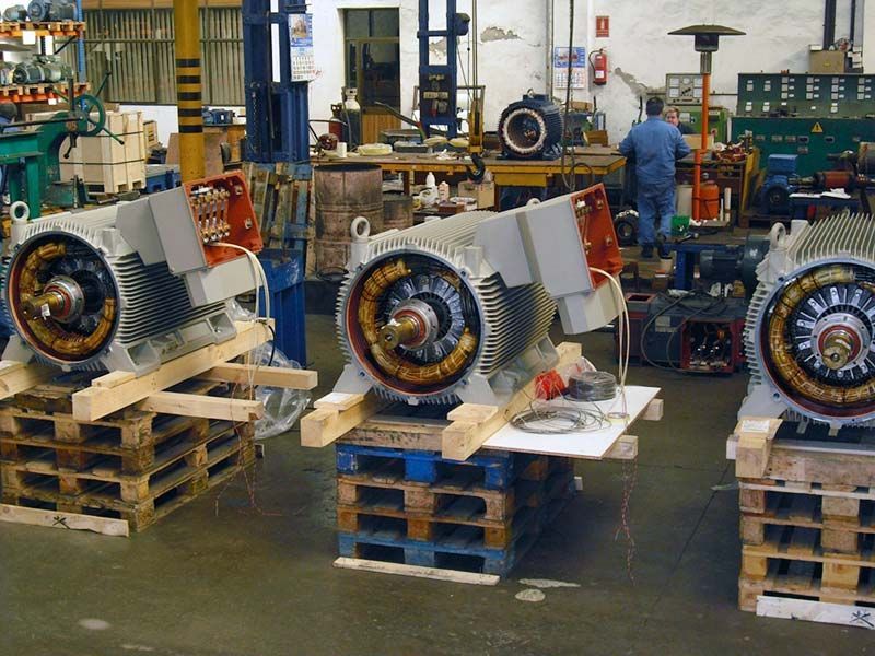 Tres motores eléctricos industriales reposan sobre palés de madera en un taller, mientras un trabajador permanece de pie al fondo.