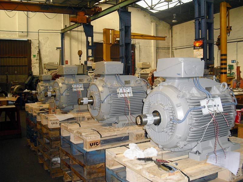 En un taller, cuatro grandes motores eléctricos grises reposan sobre palés de madera.