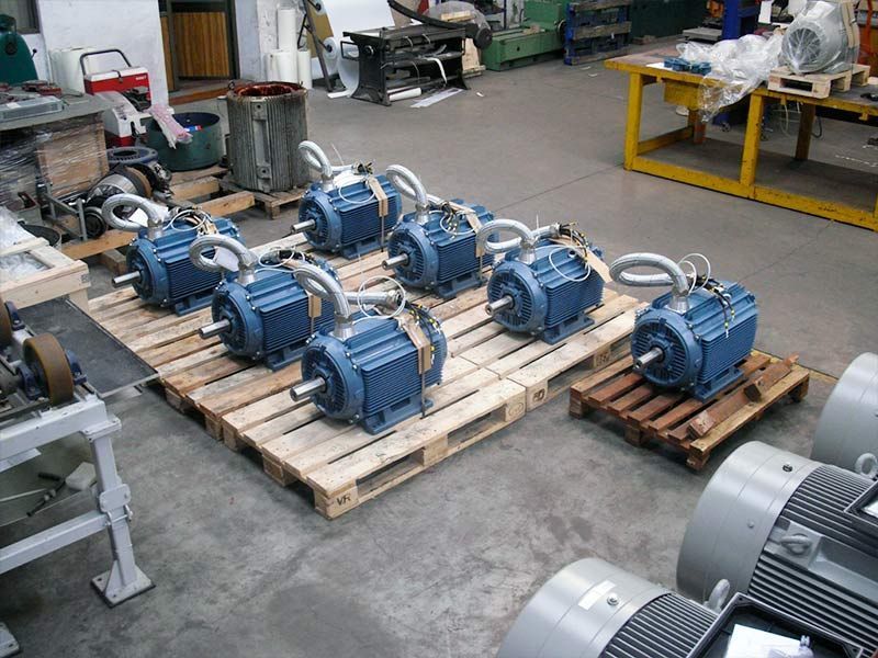 En un taller, varios motores eléctricos industriales de color azul reposan sobre palés de madera.