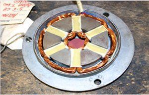 Estator de motor eléctrico con seis polos bobinados de cobre dispuestos en una carcasa circular sobre una superficie oscura.