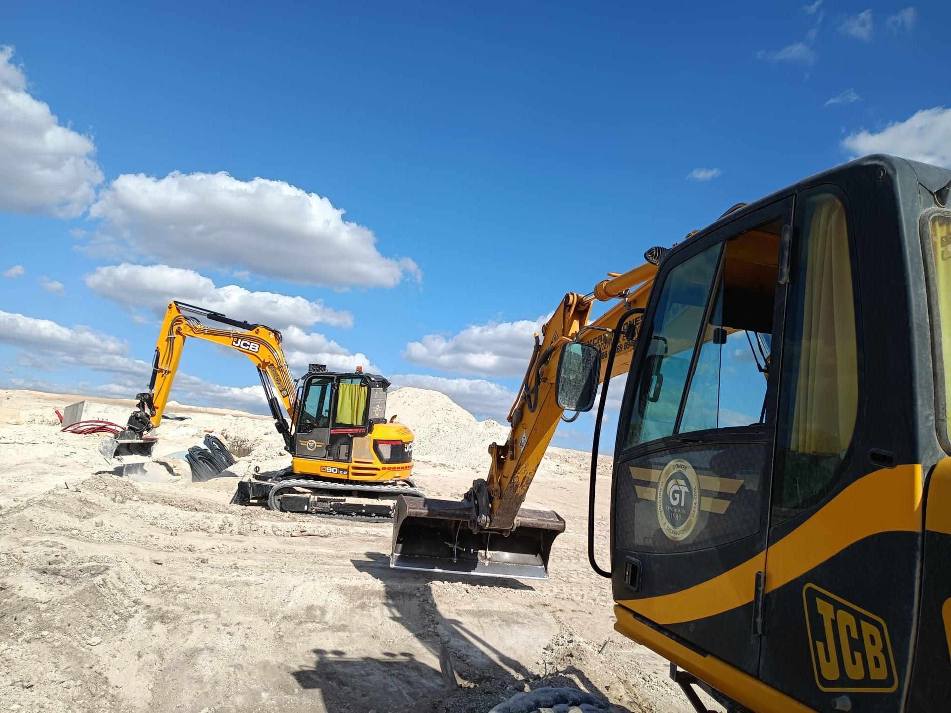 Dos excavadoras amarillas en una obra bajo un cielo azul nublado. Una de ellas está trabajando.