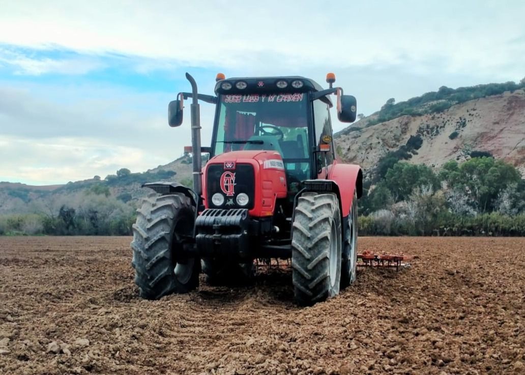 Tractor rojo arando un campo bajo un cielo nublado.