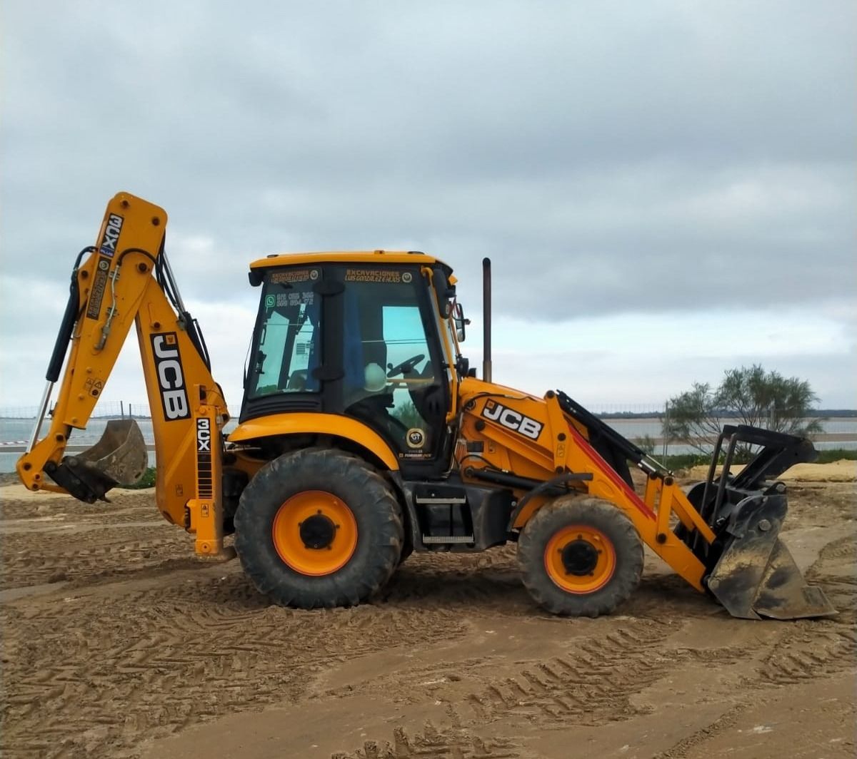 Retroexcavadora JCB amarilla en una playa de arena bajo un cielo nublado.
