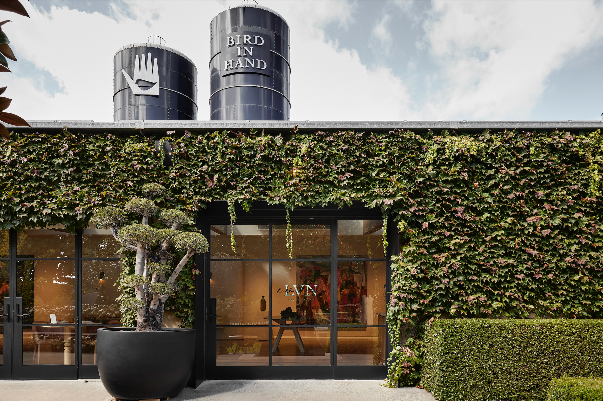 Building with green wall, glass doors, potted tree, two black tanks on roof.