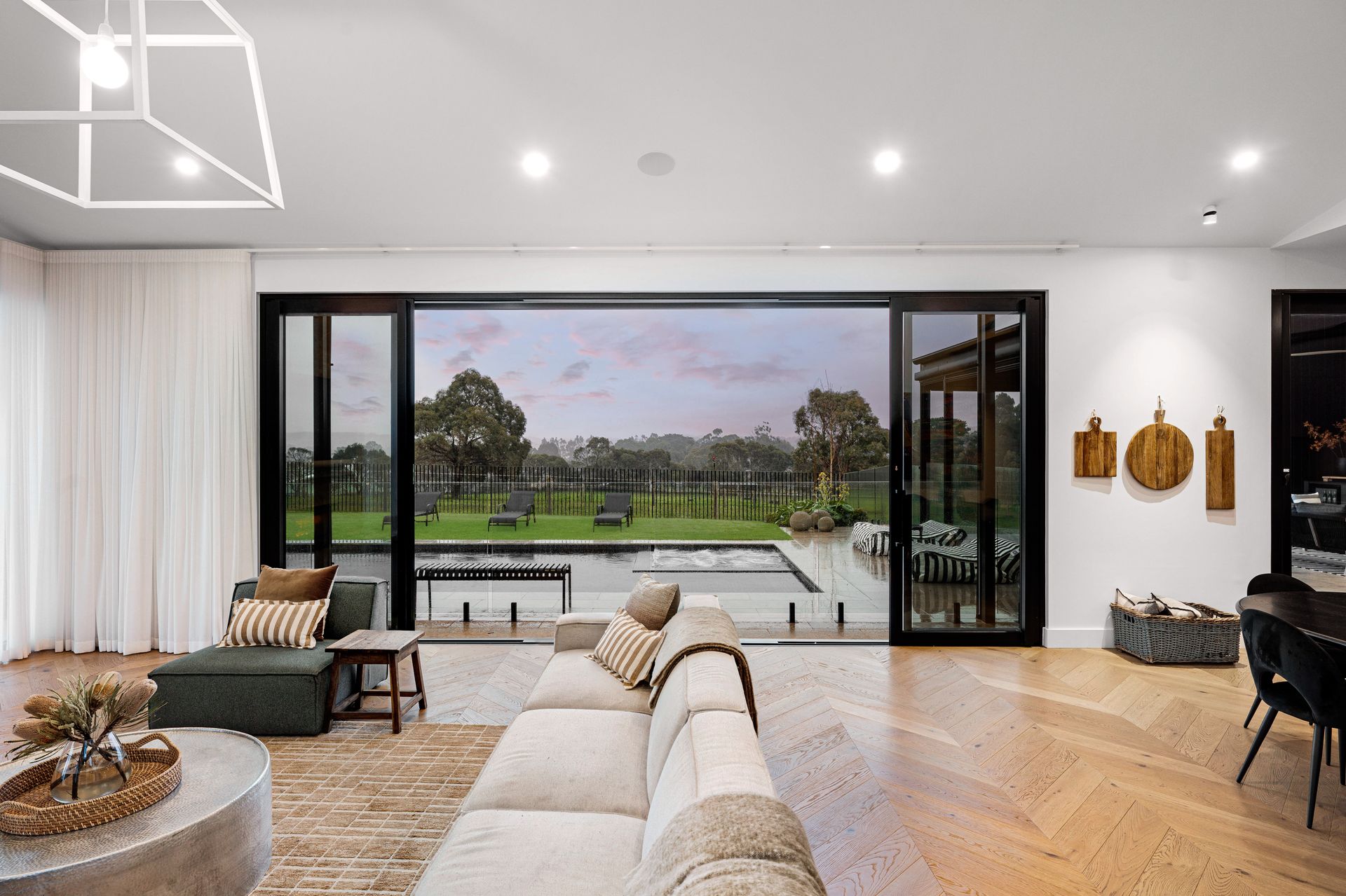 Living room with a large window overlooking a yard with a pool. Light-colored sofa, wood flooring, and decorative wall art.