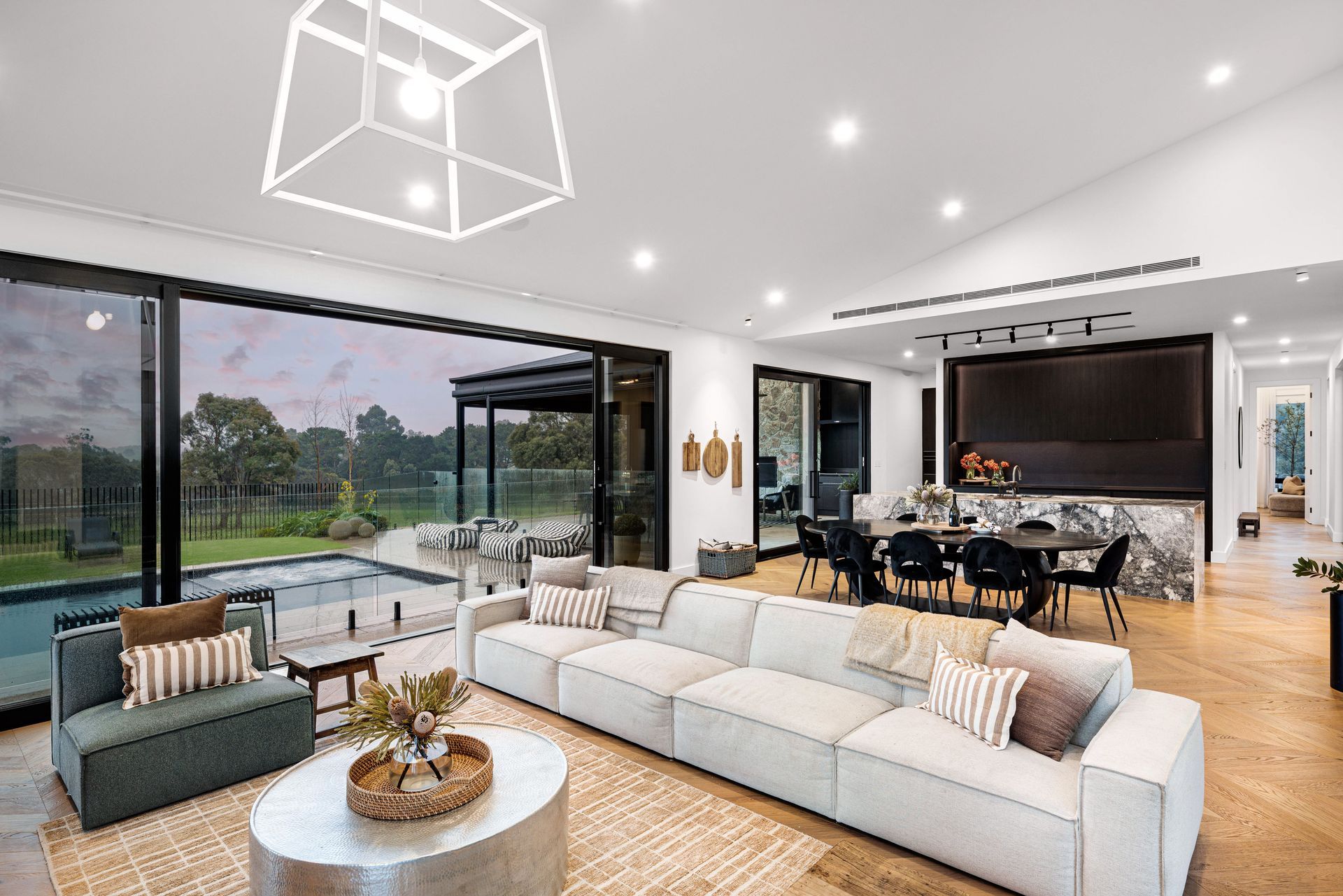 Modern living room with lake view, large sofa, dining area, and open doors to a pool.