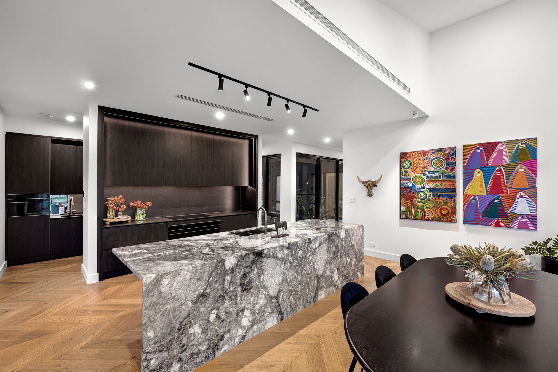 Modern kitchen with marble island, dark cabinetry, wooden floor, and colorful artwork.