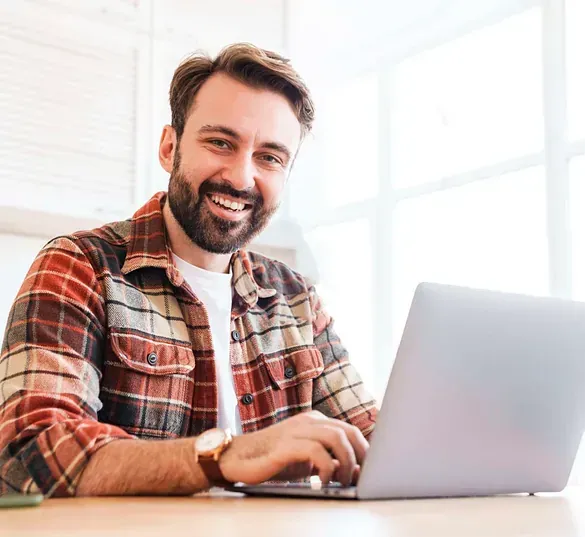 Un hombre está sentado en una mesa usando una computadora portátil.