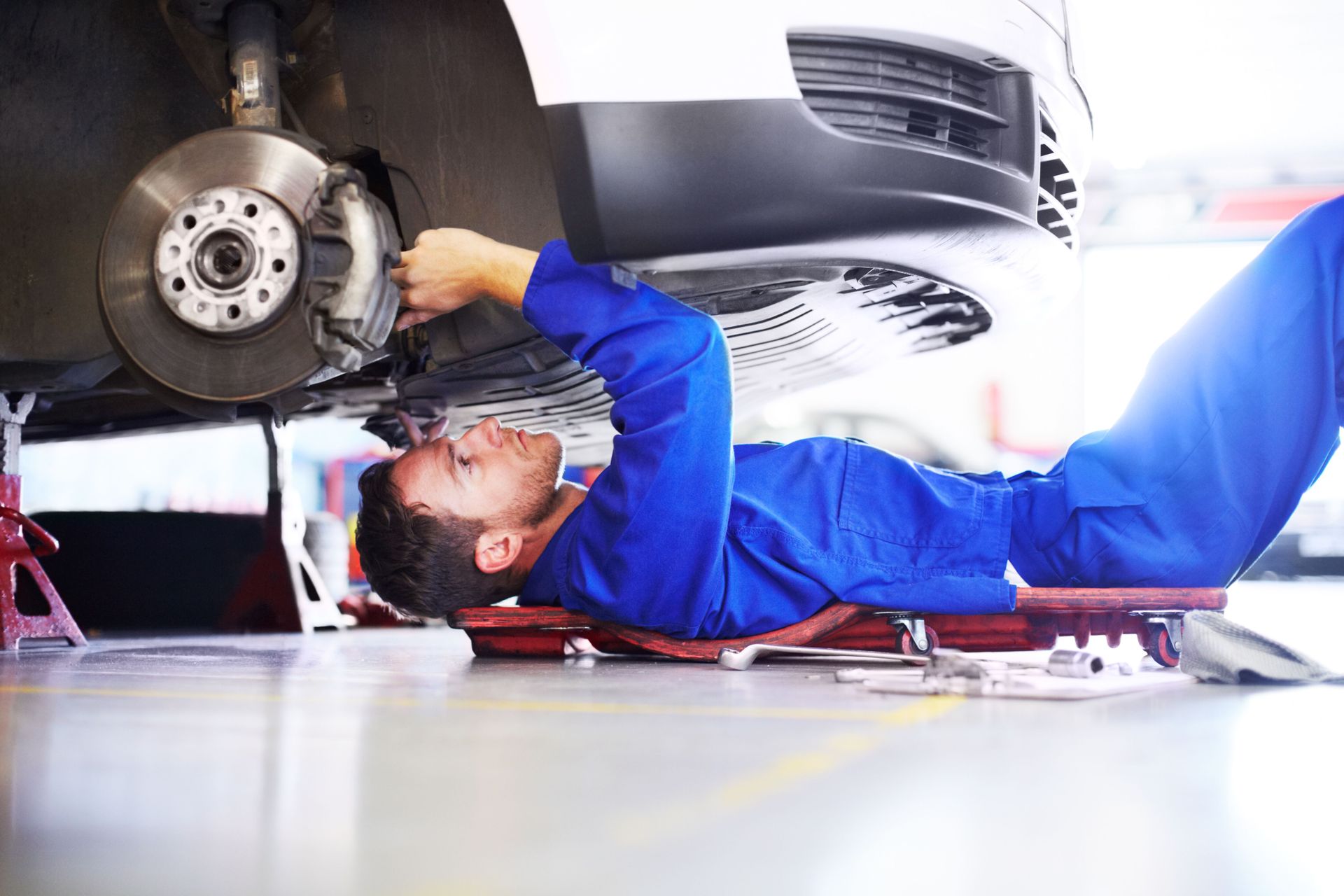 Un mecánico está tendido en una camilla debajo de un coche en un garaje.