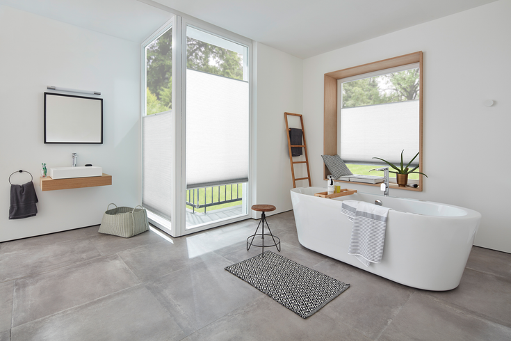 Modernes weißes Badezimmer mit freistehender Badewanne, Jalousien und Steinfliesenboden.