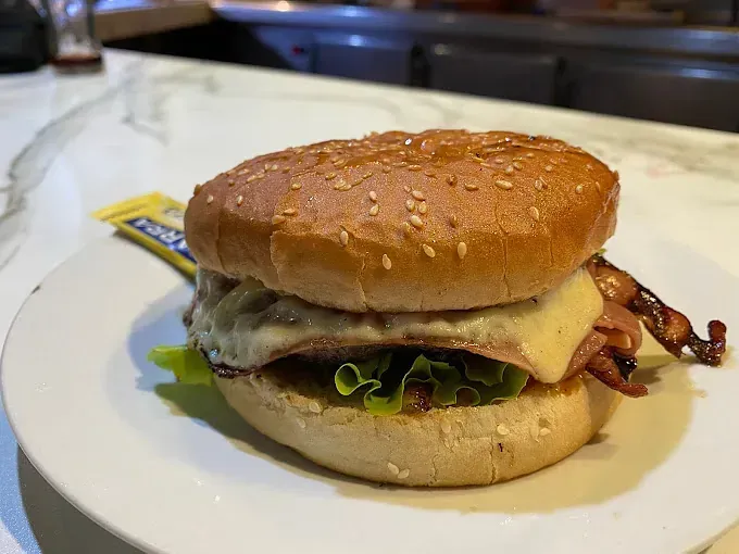 Una hamburguesa en un pan con lechuga y tocino en un plato blanco.