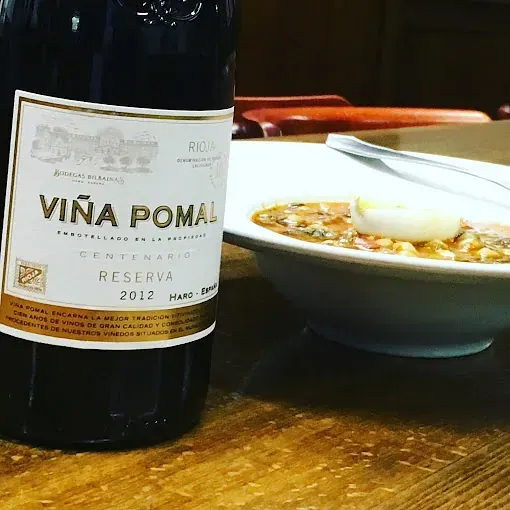 Una botella de vino viña pomal junto a un tazón de sopa