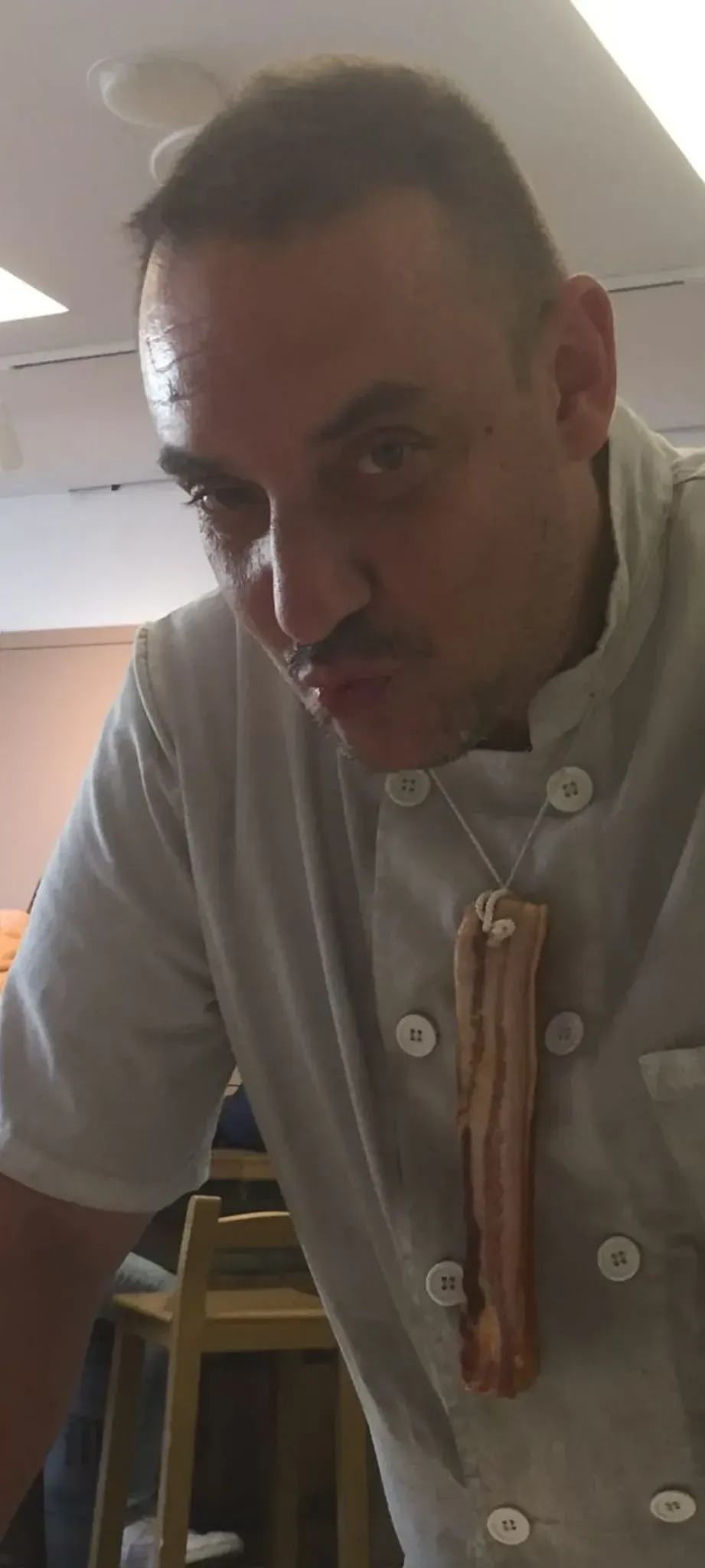 Un hombre con chaqueta de chef sostiene un trozo de tocino en su bolsillo.