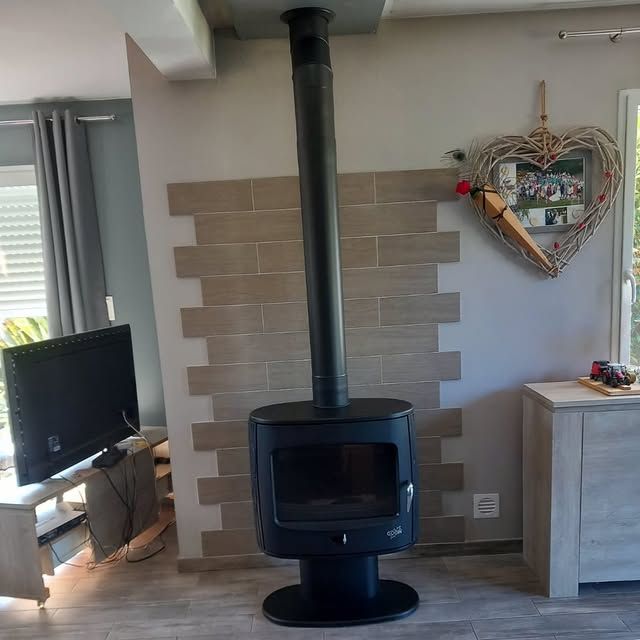 Dans un salon, un poêle à bois noir se dresse devant un mur d'accent en carrelage beige imitation brique.