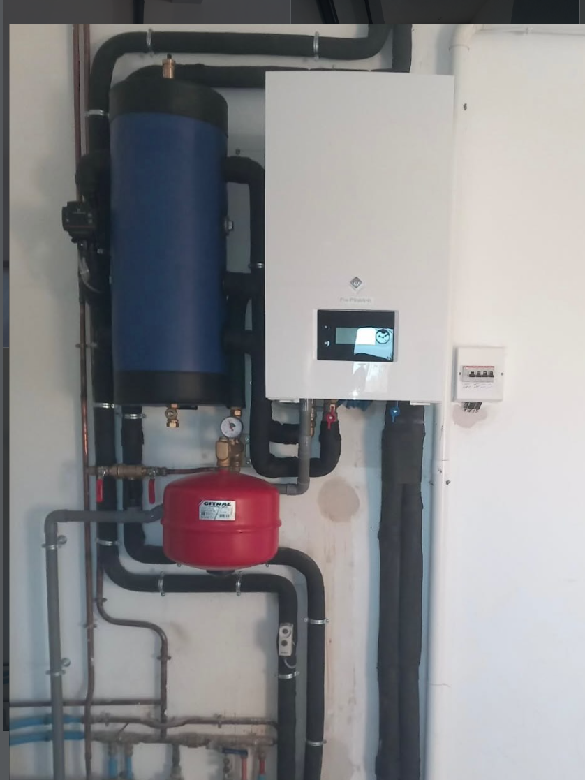 Une chaudière murale blanche, un réservoir tampon cylindrique bleu et un vase d'expansion rouge avec tuyauterie de raccordement.