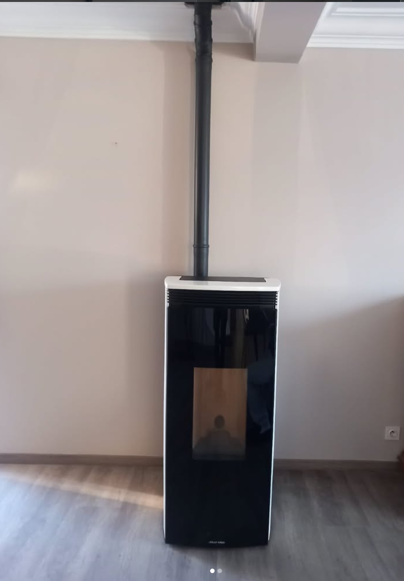Un poêle à granulés noir et blanc est adossé à un mur nu, avec un conduit de fumée en métal noir s'étendant verticalement jusqu'au plafond.