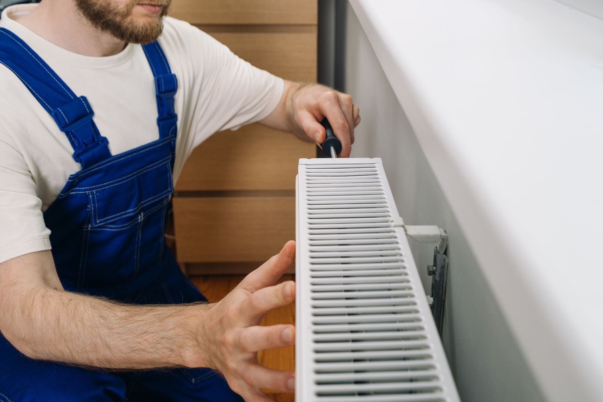 Une personne installe un radiateur blanc à l'aide d'un tournevis dans un intérieur de maison