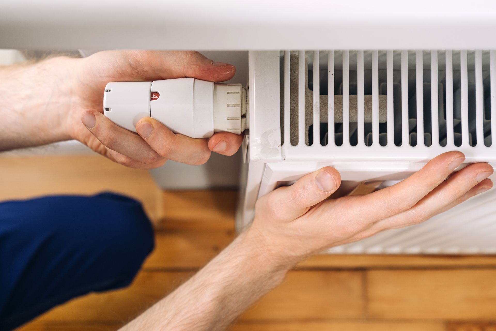Mains installant une vanne thermostatique blanche sur un radiateur dans un intérieur de maison
