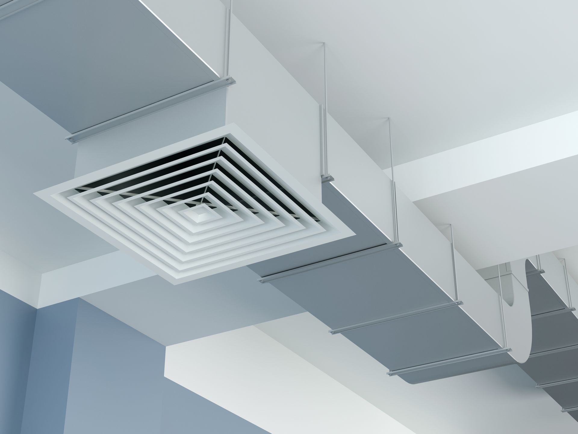 Une grille d'aération carrée blanche intégrée à un système de conduits de ventilation industriels gris, suspendu à un plafond blanc.