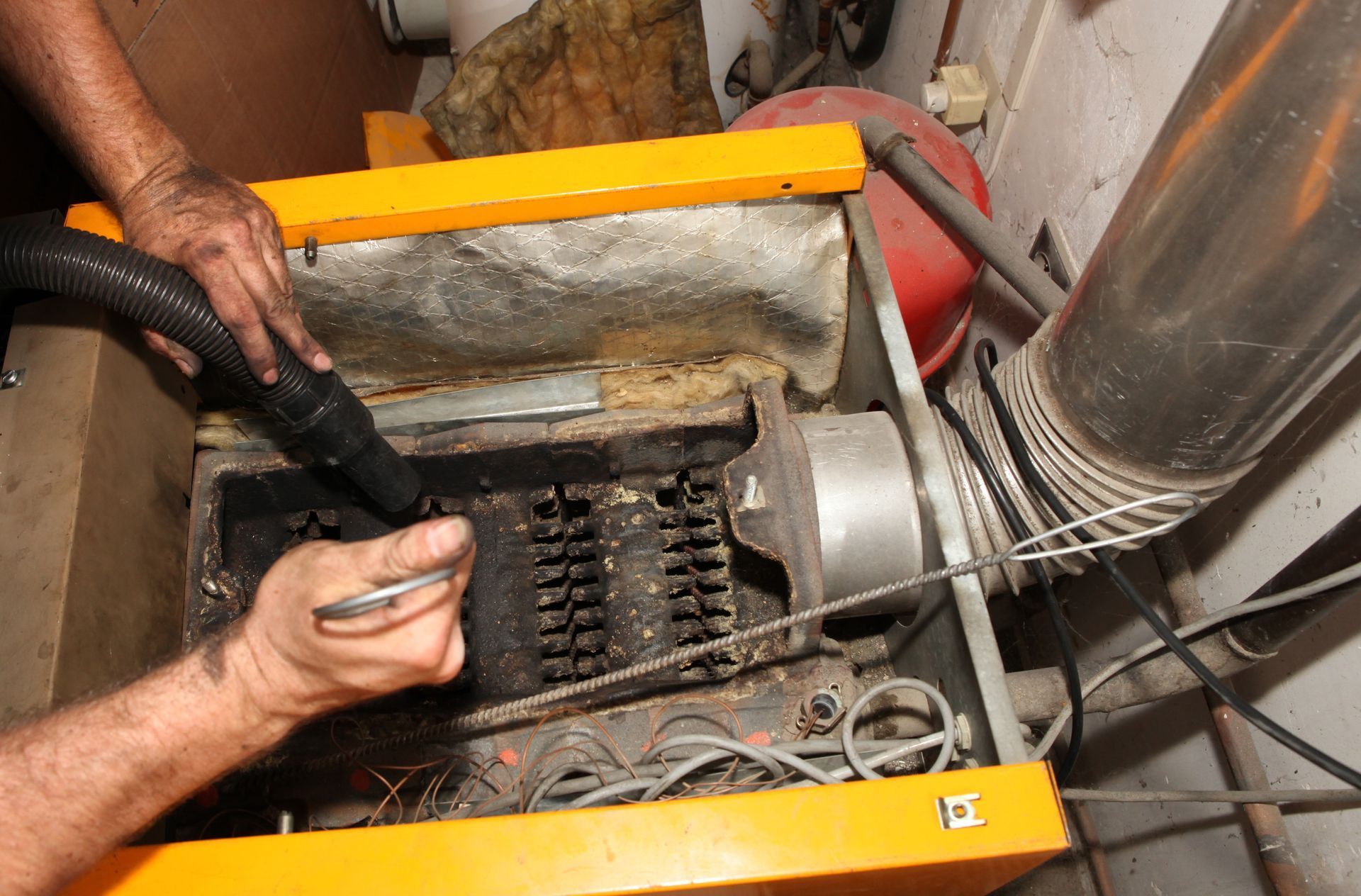 Un technicien utilise un tuyau d'aspirateur et un outil manuel pour nettoyer les composants internes d'une chaudière.