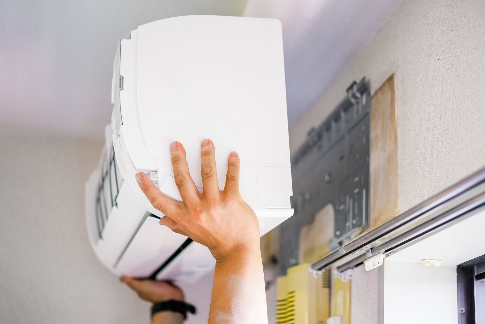Une personne installe un climatiseur mural à l'intérieur d'une pièce.
