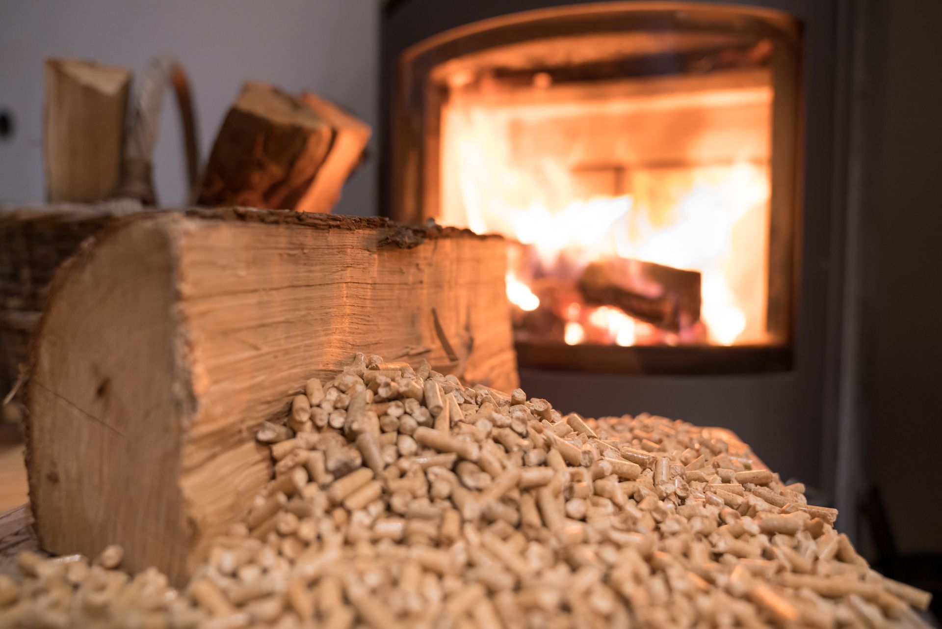 Un tas de granulés de bois clairs est posé à côté d'une bûche devant une cheminée incandescente.