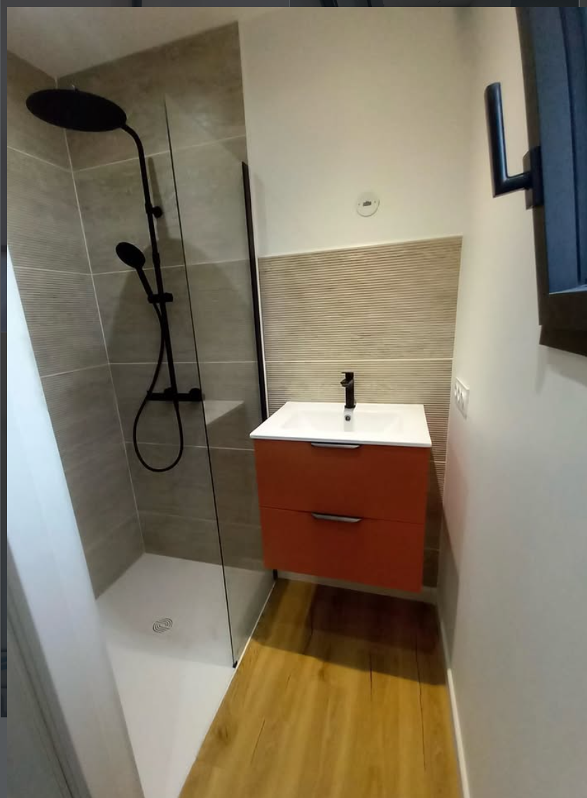 Une petite salle de bains avec une douche vitrée, un meuble-lavabo orange fixé au mur avec un lavabo blanc et un parquet clair.