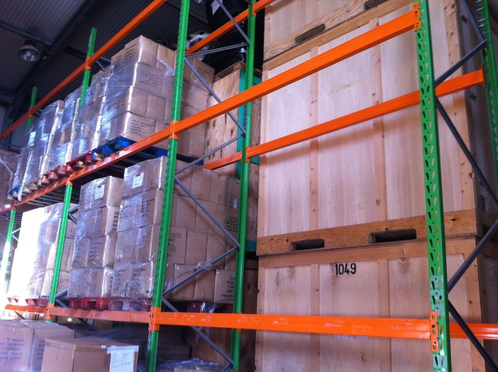 Rayonnages d'entrepôt avec des palettes filmées et des caisses en bois empilées dans des rayonnages orange et verts