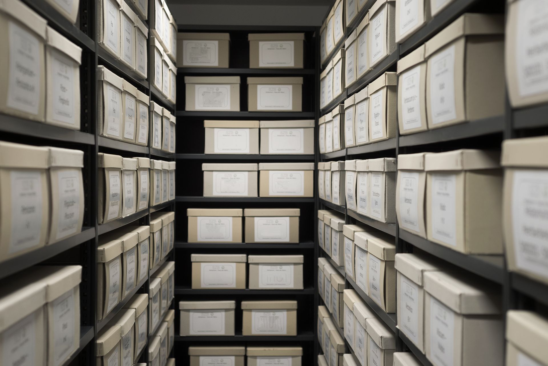 Des rangées de boîtes d'archives étiquetées sur des étagères dans une allée de stockage étroite.