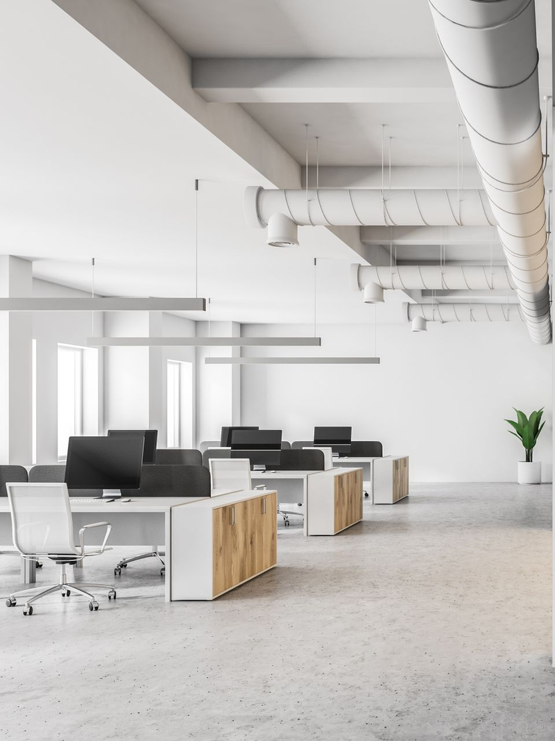 Bureau moderne et lumineux à aire ouverte avec bureaux blancs, écrans noirs et une plante près des grandes fenêtres