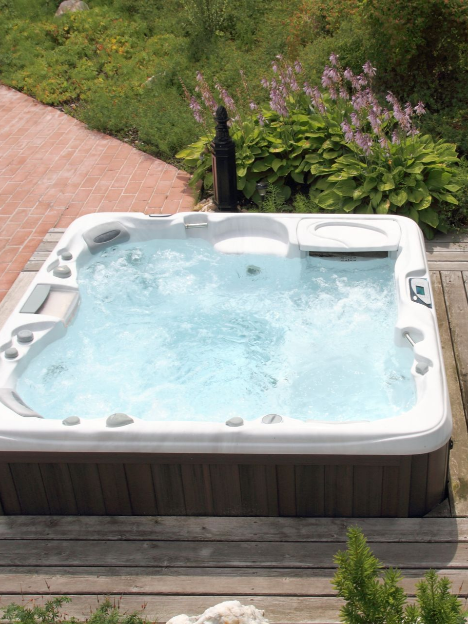 Jacuzzi dans le jardin avec eau bouillonnante, à côté d'une terrasse en bois et de fleurs de jardin.
