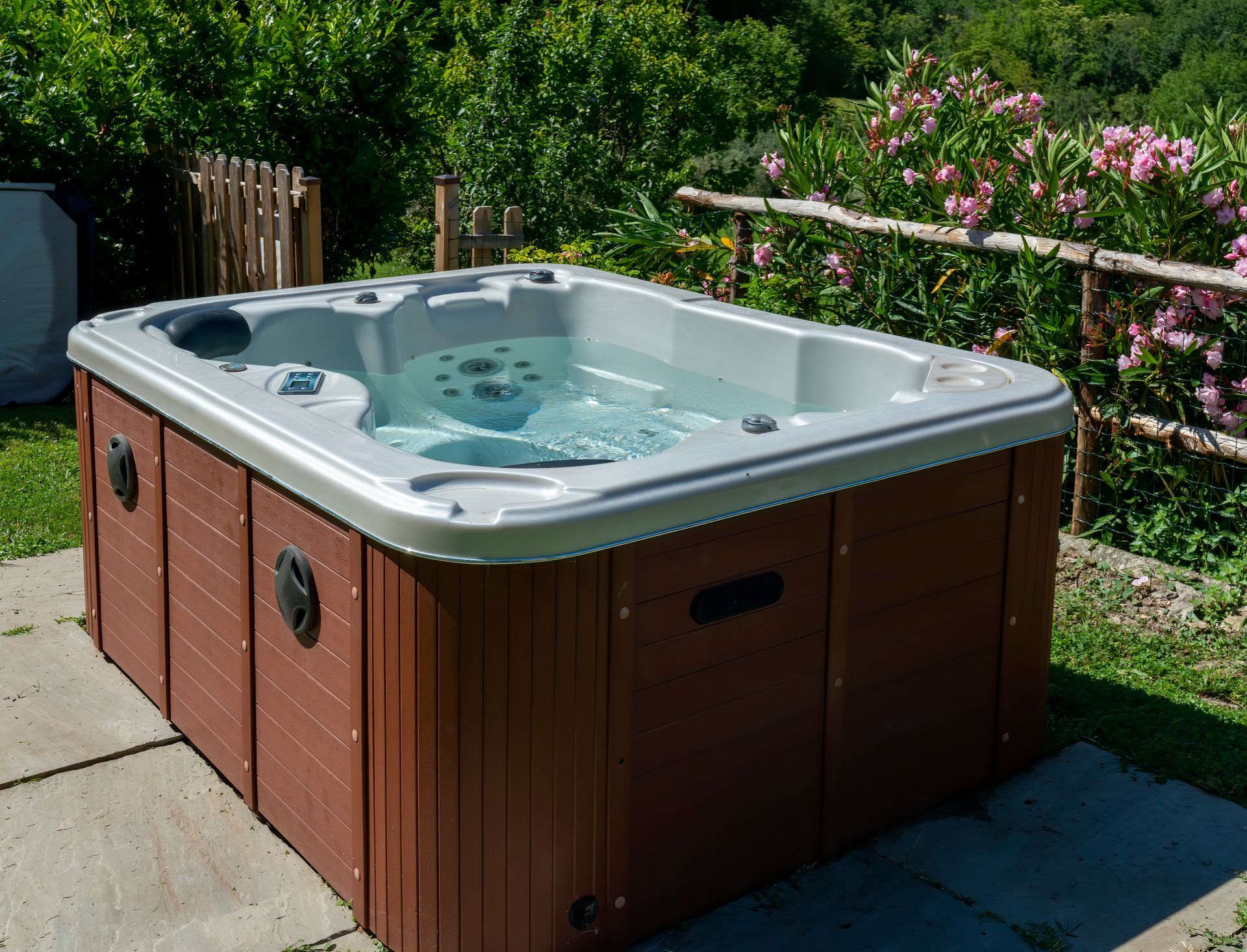 Jacuzzi dans un jardin avec eau bouillonnante sur une terrasse en béton, entouré de verdure et de fleurs.