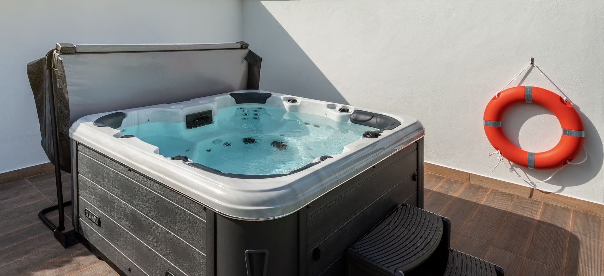 Jacuzzi gonflable à l'eau bleue sur une terrasse en bois à côté d'une bouée de sauvetage orange